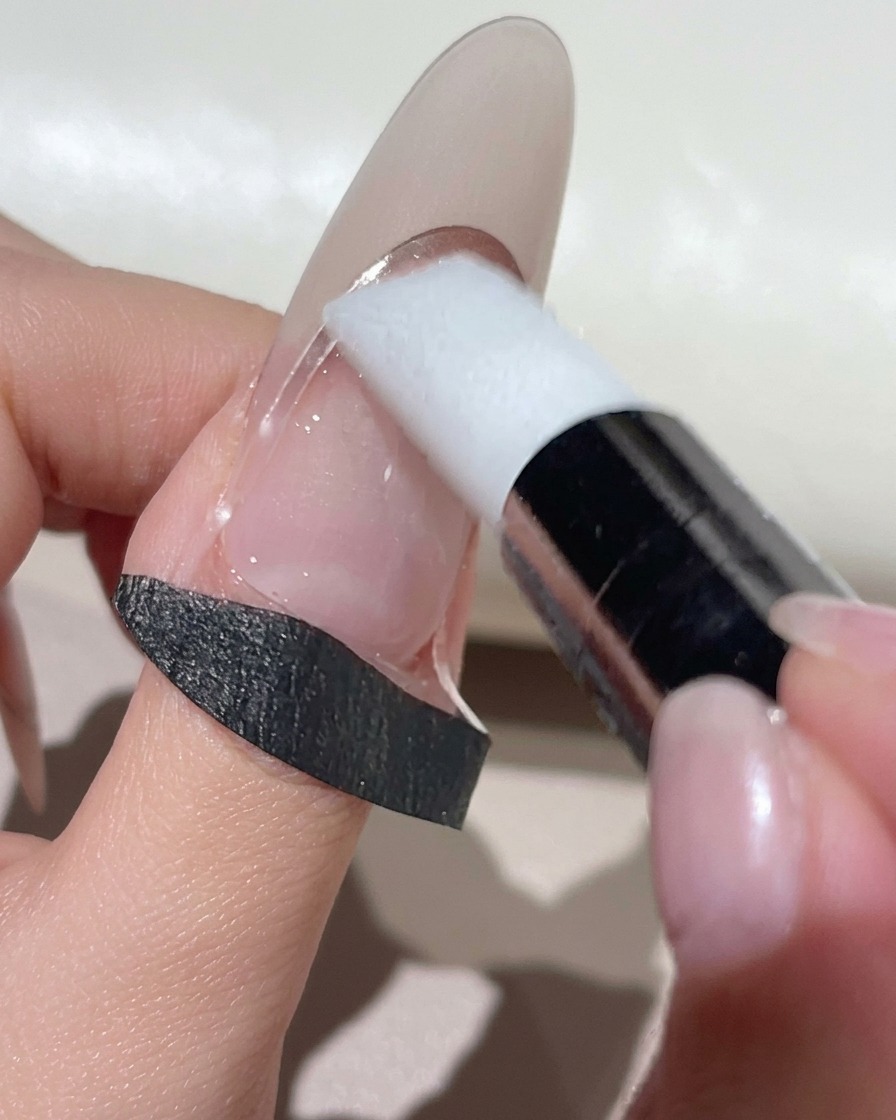 Uno strumento per make-up in silicone bianco che preme un adesivo guida French curvo su ununghia dal tono naturale.