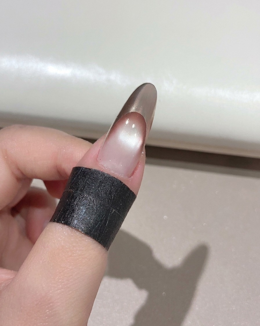 Un pennello per unghie che applica un top coat lucido trasparente su una manicure French oro rosa finita.
