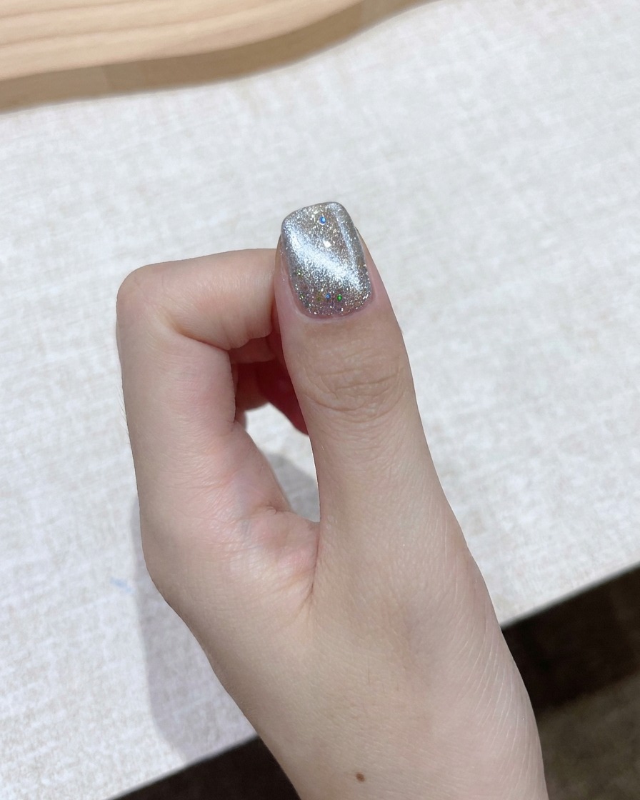 Un blocco magnetico rettangolare tenuto vicino a ununghia in gel cat-eye brillante per formare un fascio aurora luminoso.