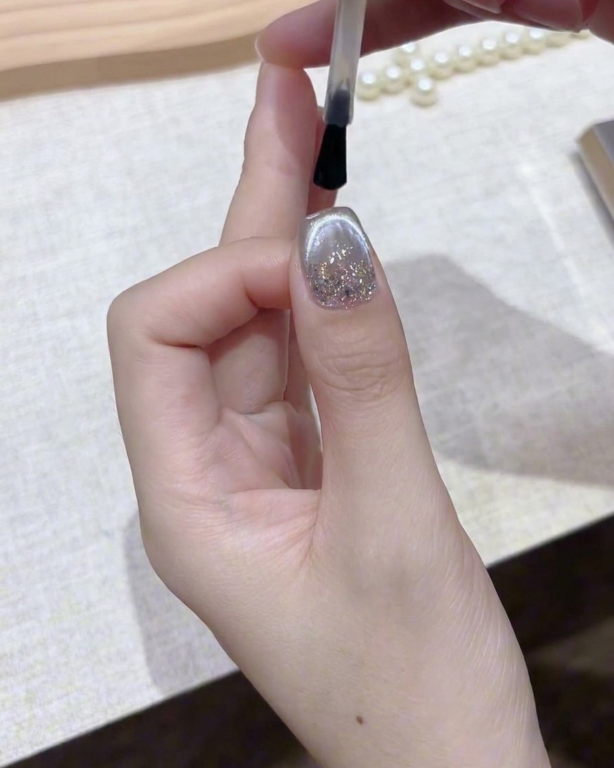 Un pennello che applica un top coat trasparente e lucido su ununghia in gel magnetico argentato finita.