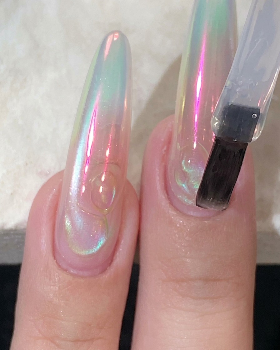 Un pennello per unghie piatto che applica un top coat trasparente e lucido su ununghia lunga ricostruita.