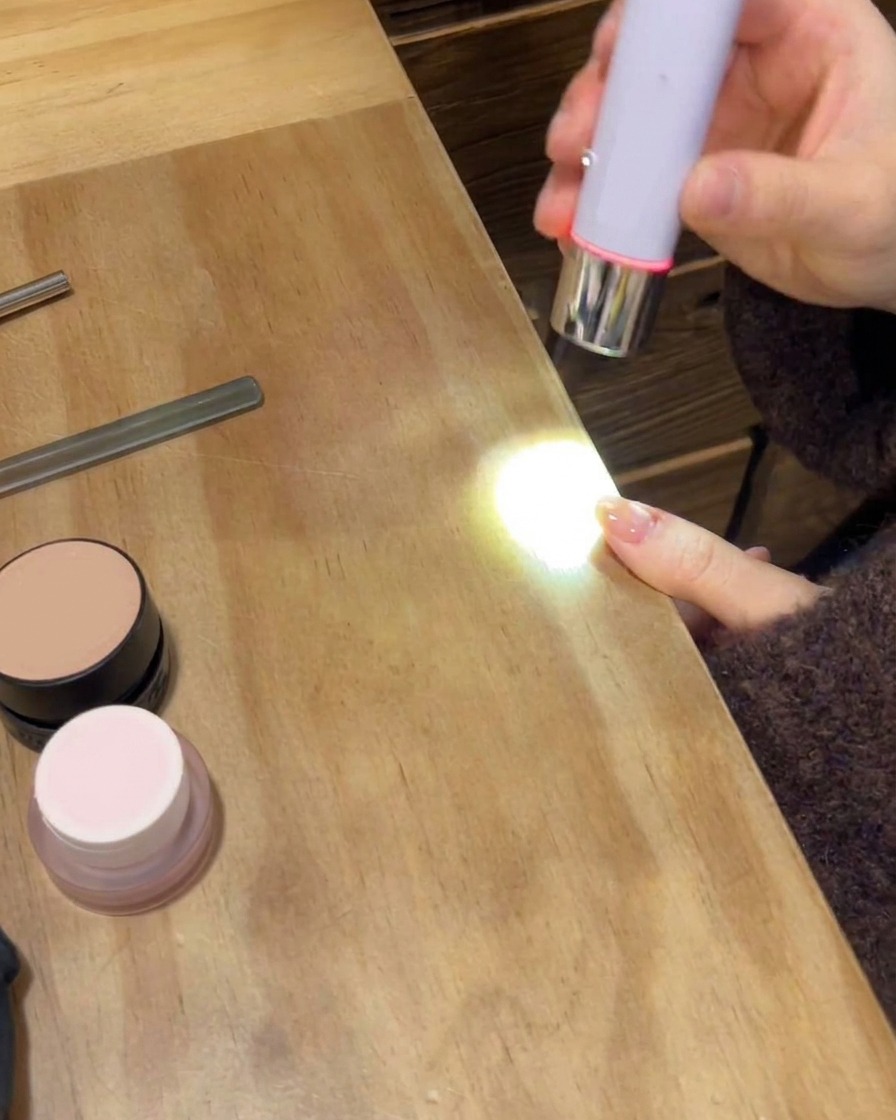 Una lampada UV/LED portatile polimerizza il top coat finale lucido su una mano con manicure.