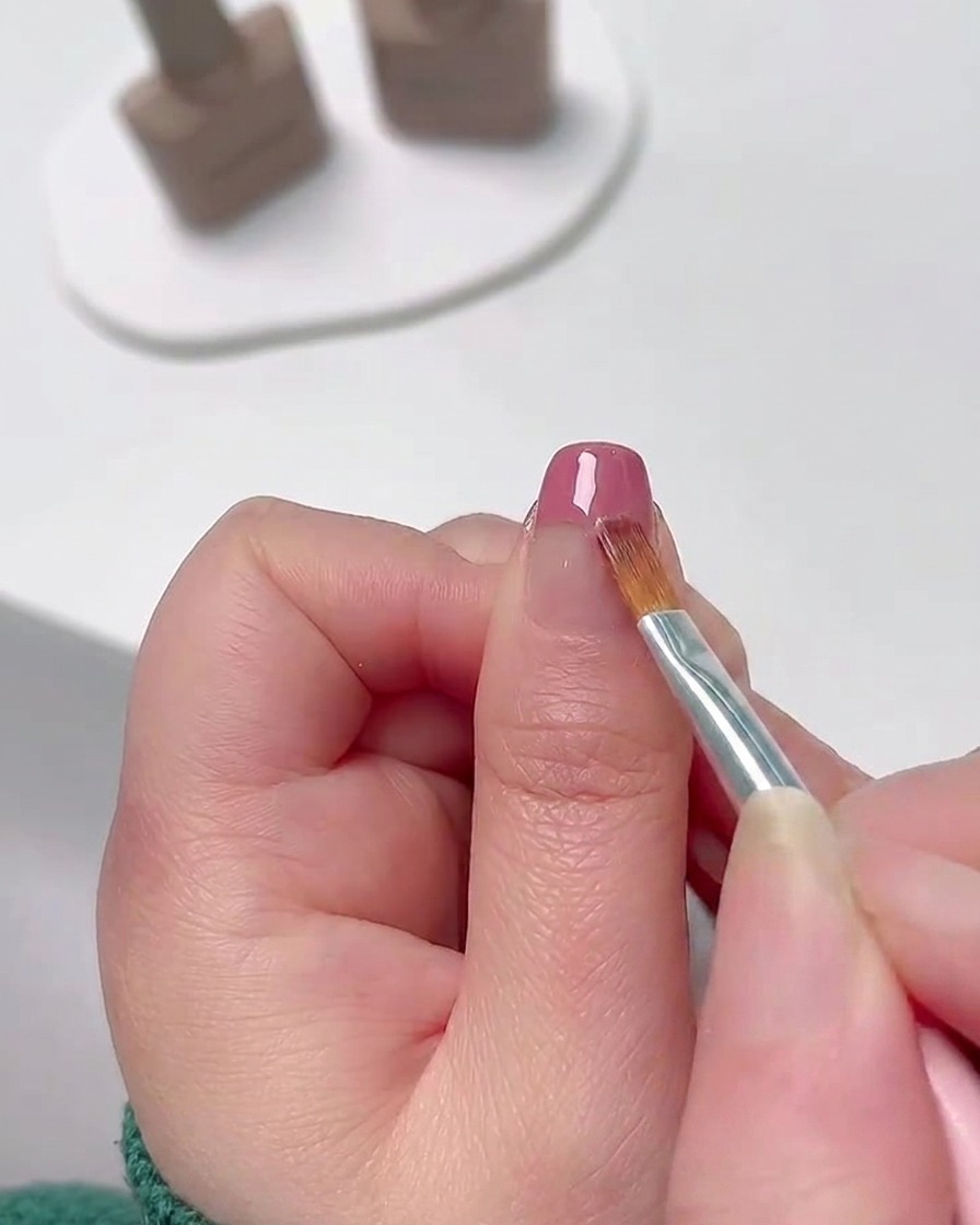 Primo piano di un pennello fine per nail art che sfuma lo smalto gel rosa dalla punta dellunghia verso il basso per creare una delicata sfumatura di colore.