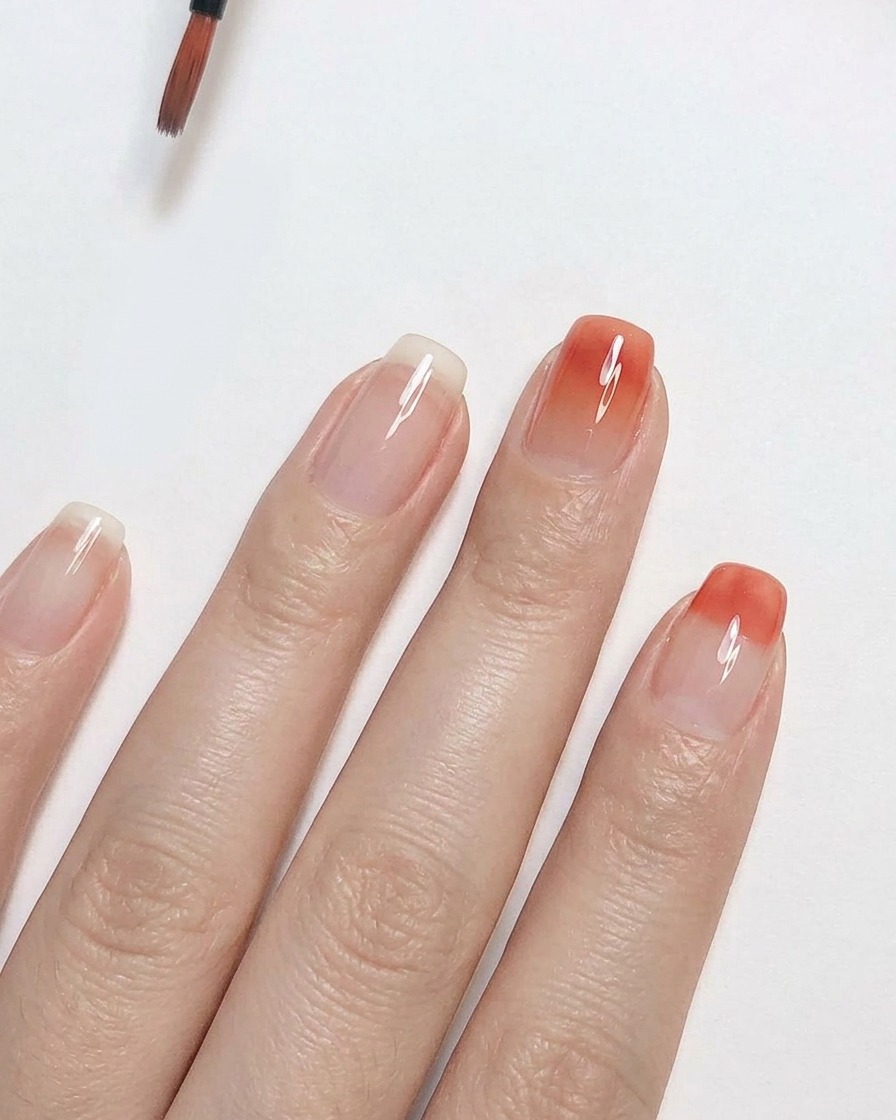 Un pennello di precisione sfuota lo smalto gel rosa pesca verso lalto su ununghia trasparente per creare un effetto gradiente ombré uniforme.