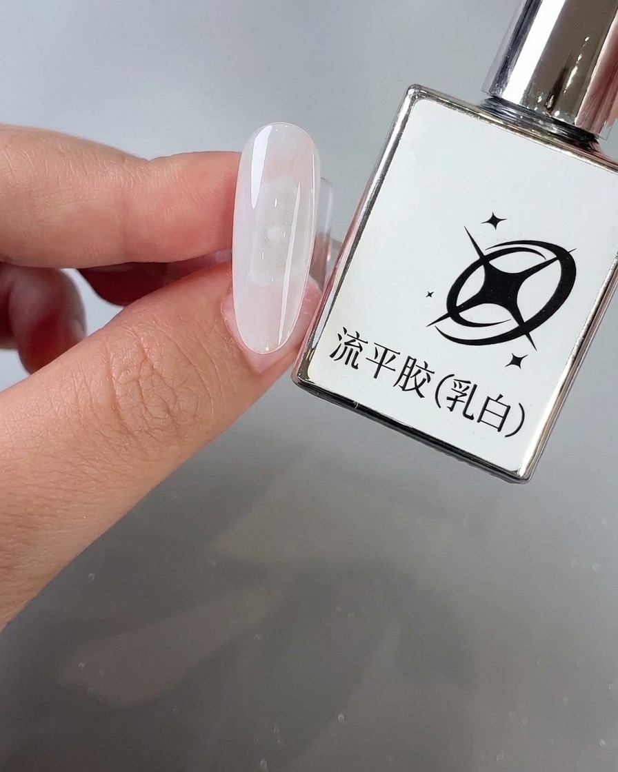 Un pennello che applica il gel autolivellante bianco latte sulla superficie di ununghia a mandorla accanto al flacone del prodotto.