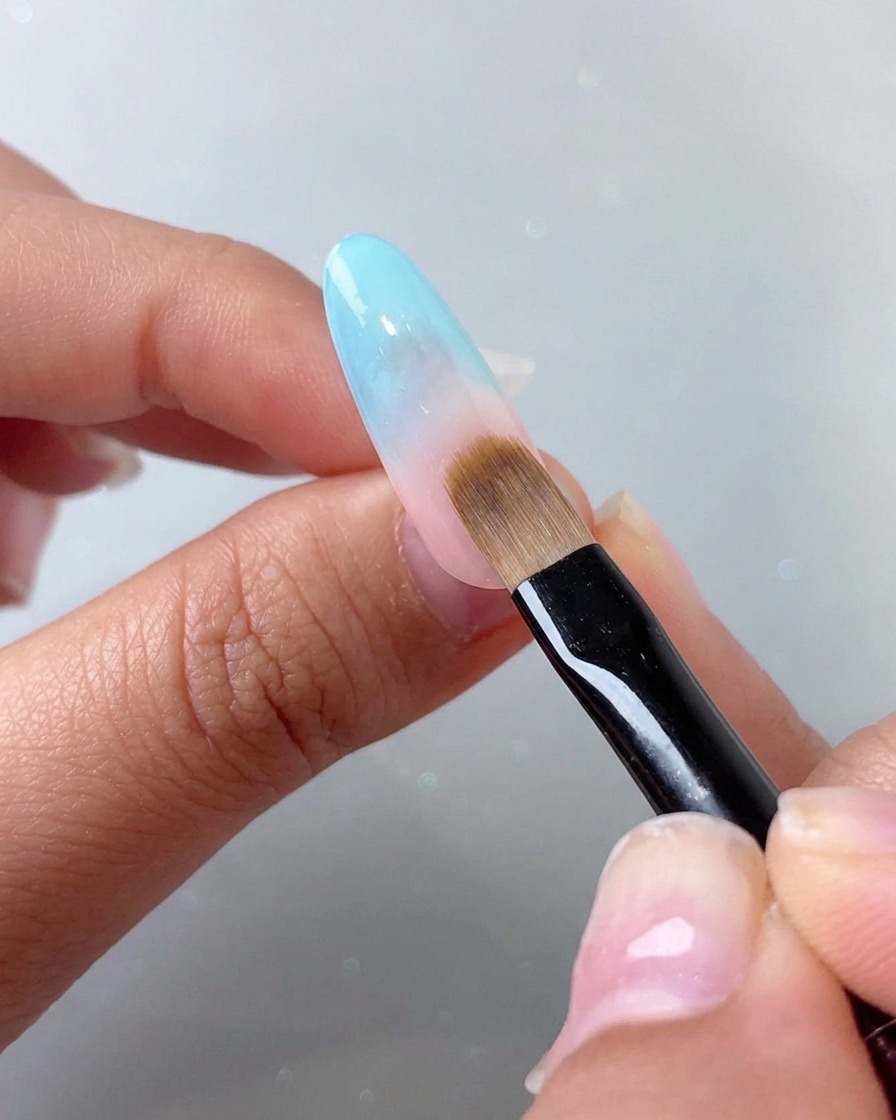 Un pennello da tamponamento che sfuma un effetto gradiente blu sulla porzione superiore rosata dellunghia.