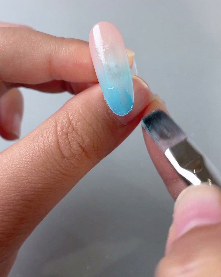Un pennello che applica un secondo strato di gel vetro blu sulla metà anteriore della punta dellunghia.