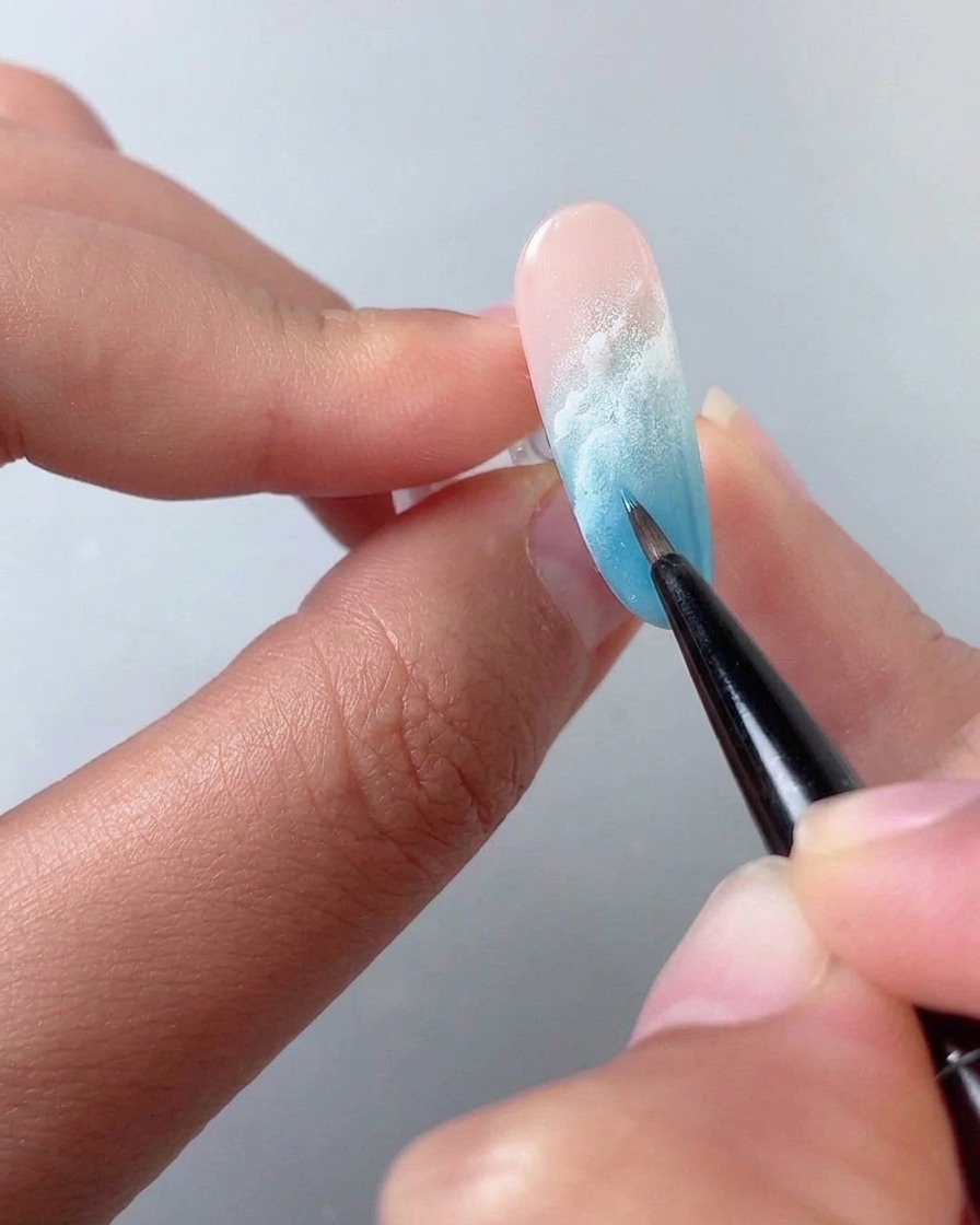 Un pennello fine che sfuma il liquido blooming bianco su ununghia sfumata di blu e rosa.