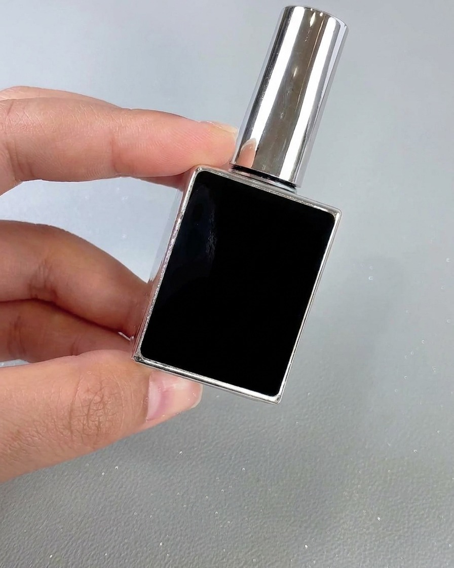 Un flacone quadrato nero e argento di top coat per unghie tenuto in mano su uno sfondo neutro.