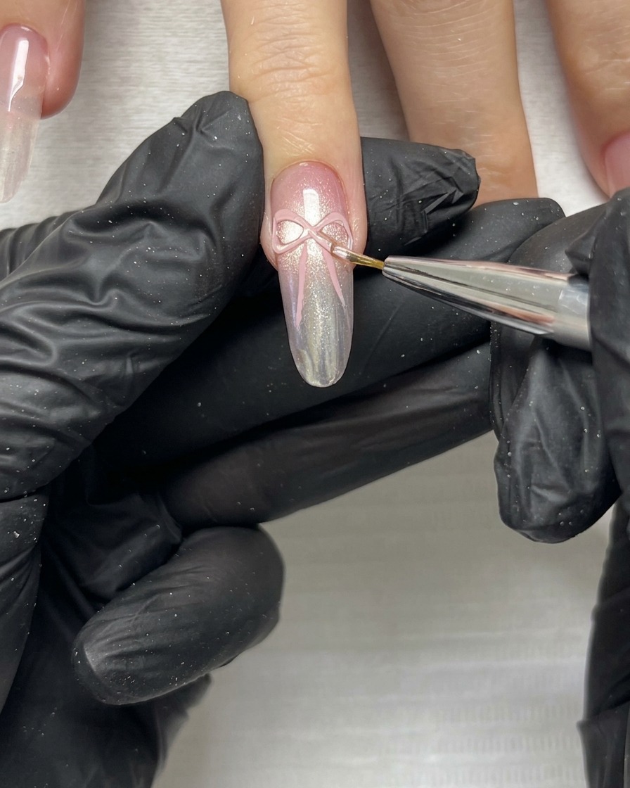 Nahaufnahme eines feinen Pinsels, der die zarten Kanten und Enden einer rosa 3D-Schleife auf einem manikürten Nagel verfeinert.