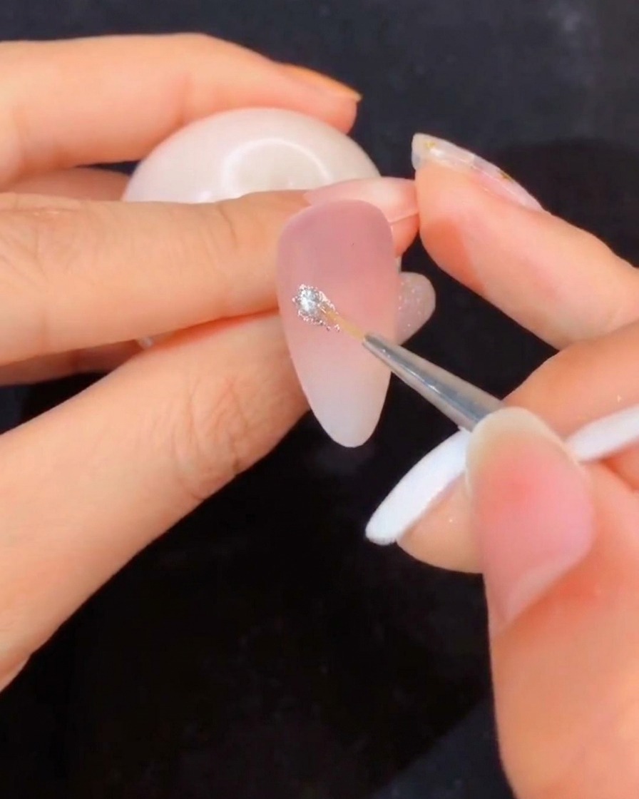 Un primo piano di un pennello sottile che si intinge in un barattolo aperto di gel da modellaggio trasparente.