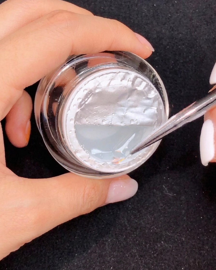 Un pennello sottile che tira una lunga forma a goccia di gel trasparente su ununghia rosa sfumata.