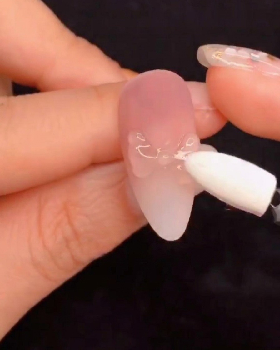 Un applicatore in spugna di silicone che sfrega la polvere di pigmento aurora su un design per unghie scolpito.