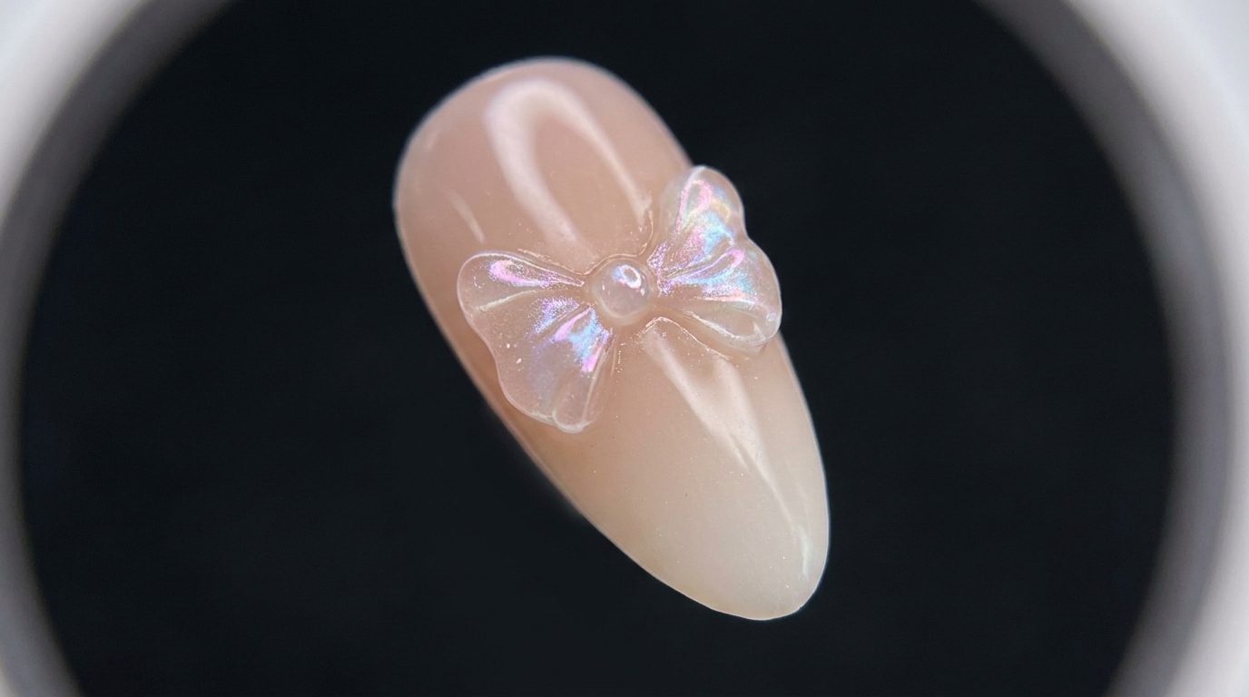 Ununghia a mandorla finita con un delicato fiocco 3D trasparente e riflessi cromati luminosi su una base sfumata da nude a bianco.