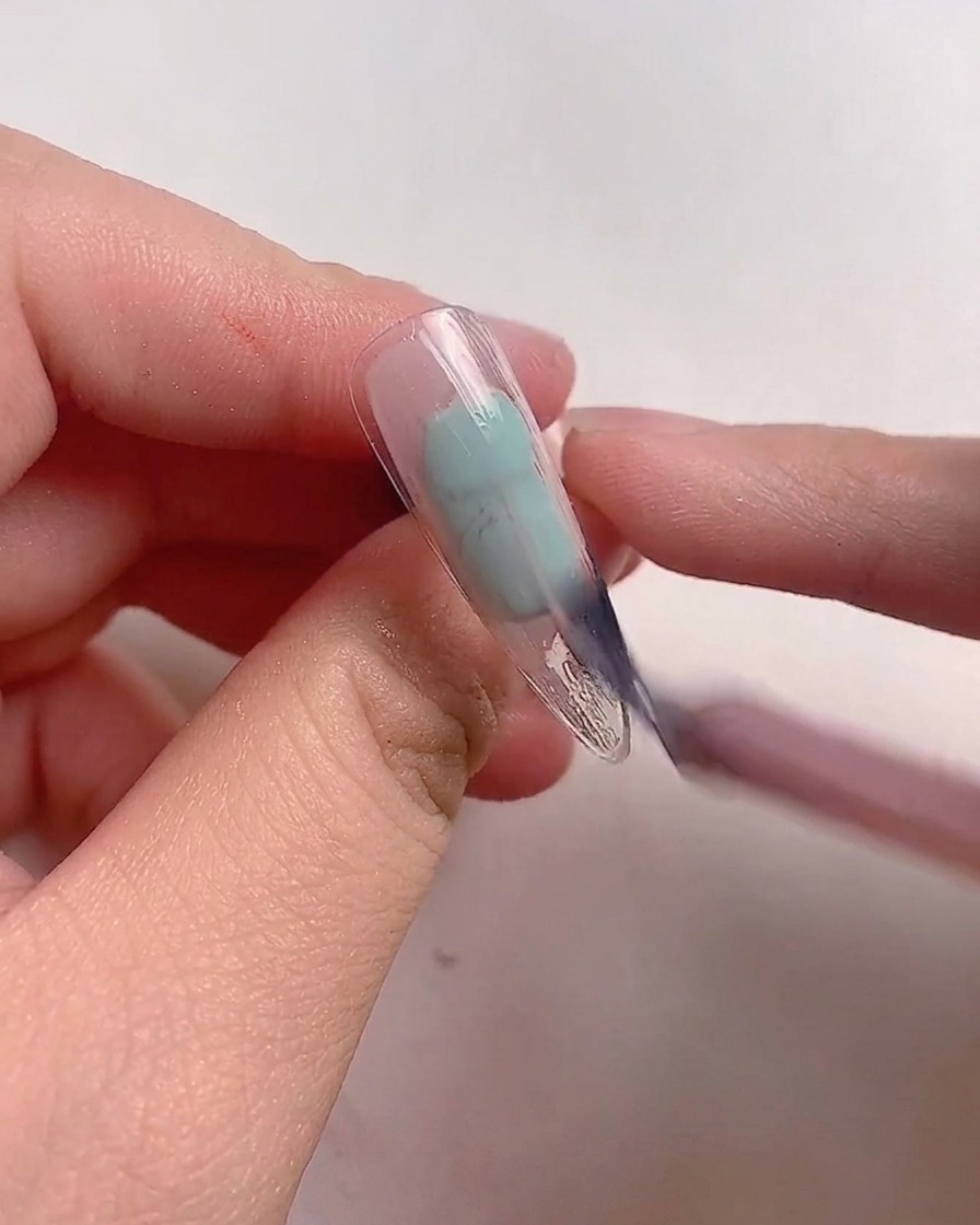 Un pennello applica lo smalto gel rosa malva su una tip per unghie trasparente.