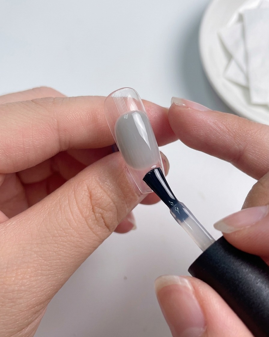 Un pennello applica uno strato di top coat su ununghia colorata.