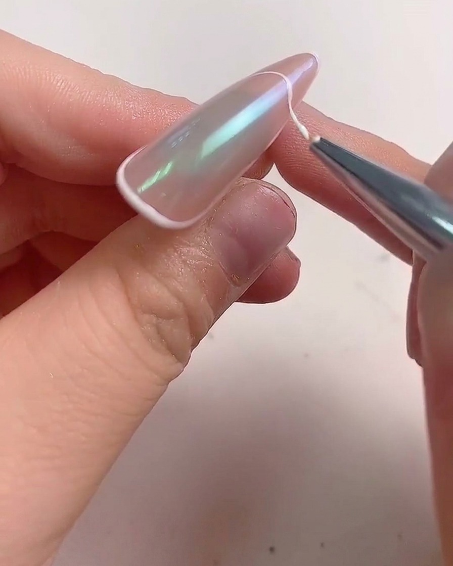 Un pennello sottile traccia una linea di gel bianco lungo il bordo di ununghia a mandorla per creare una french.