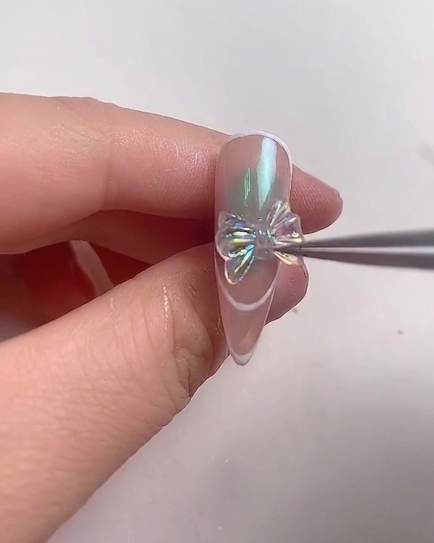 Un paio di pinzette di metallo posiziona con cura uno scintillante fiocco di cristallo iridescente al centro di ununghia a mandorla.
