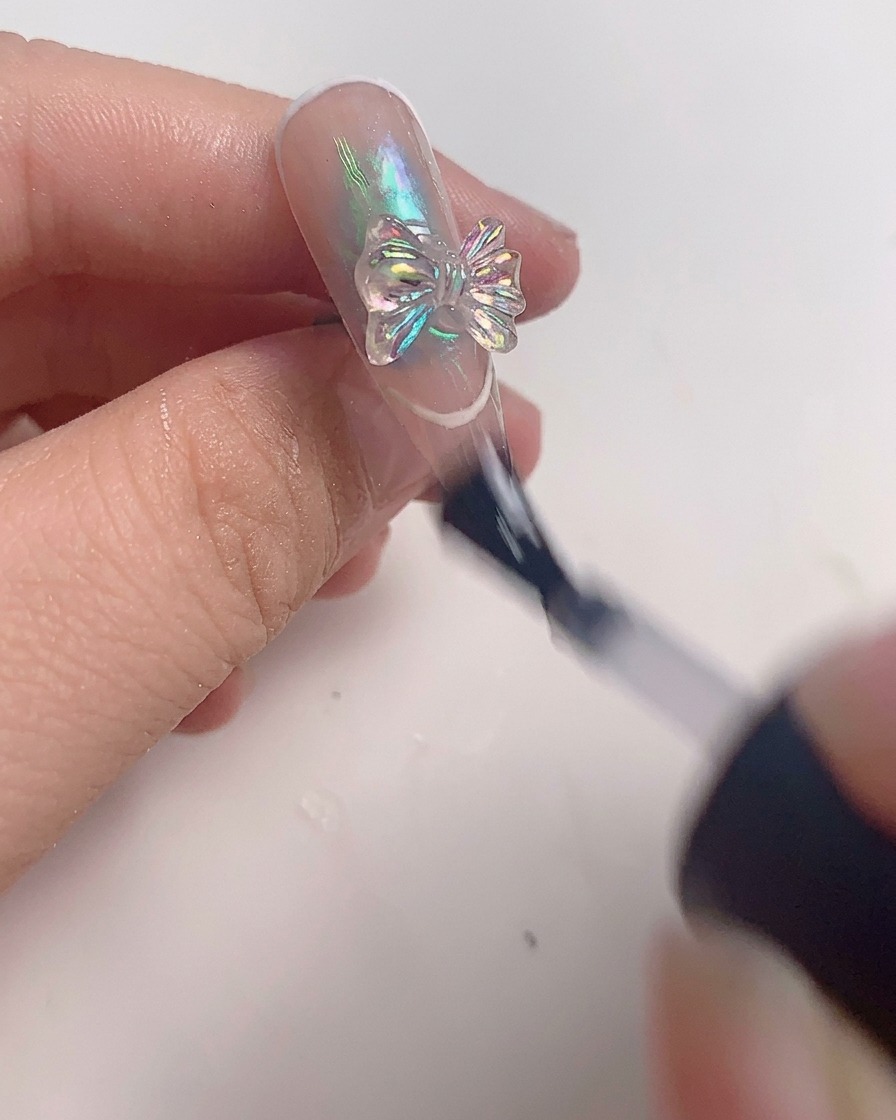 Un pennello applica uno strato finale di top coat trasparente attorno a un fiocco di cristallo su ununghia finita.