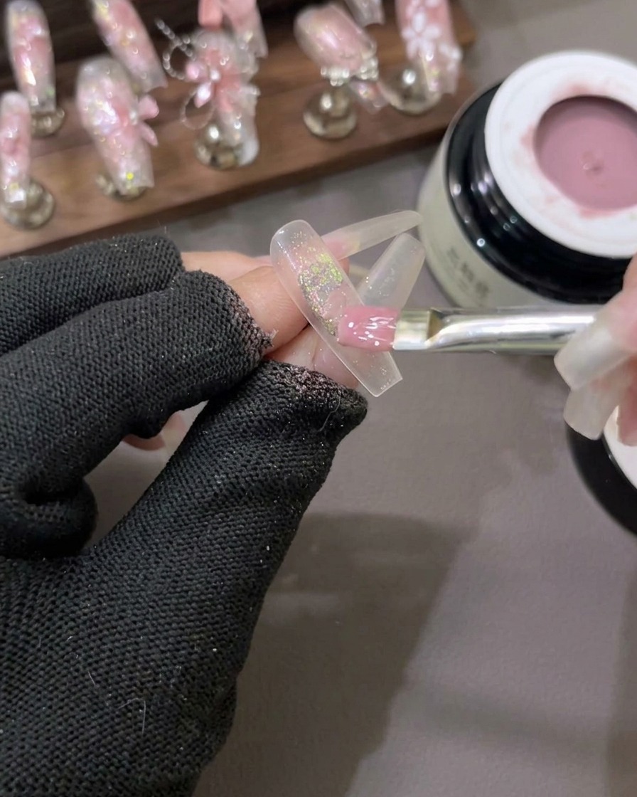 Un pennello piatto stende uno smalto gel rosa lattiginoso semitrasparente su ununghia con scaglie di glitter al centro.