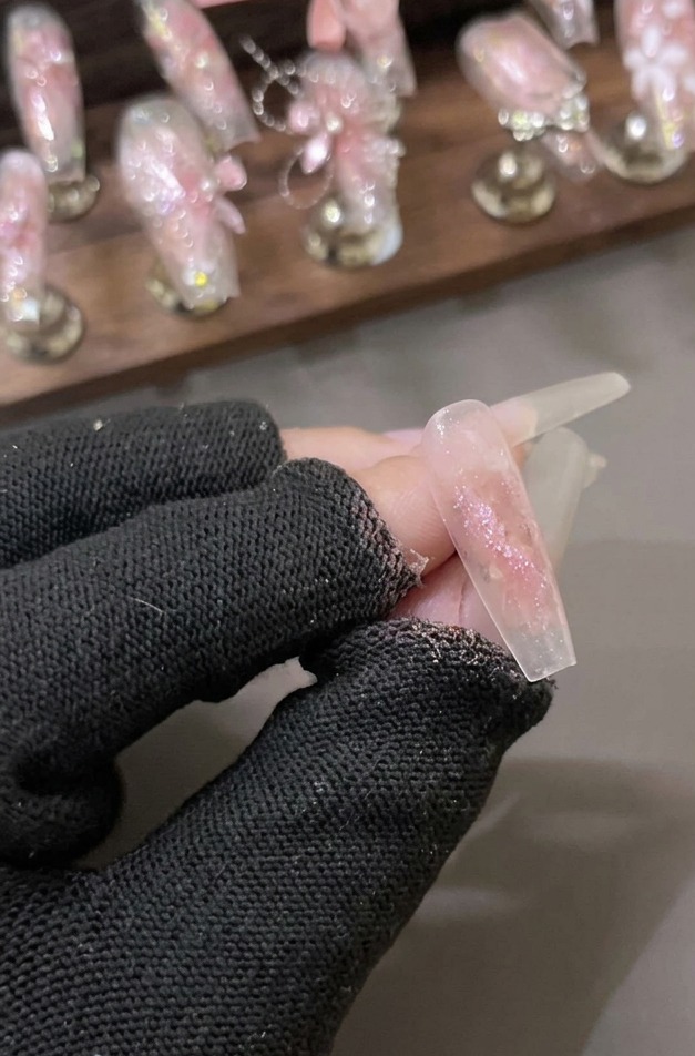 Una mano con guanto tiene ununghia trasparente rivestita con uno strato scintillante di gel glitterato rosa effetto diamante.