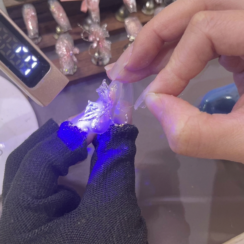 Una mini lampada UV emette luce viola su unala di farfalla 3D in gel rosa appena modellata su ununghia.