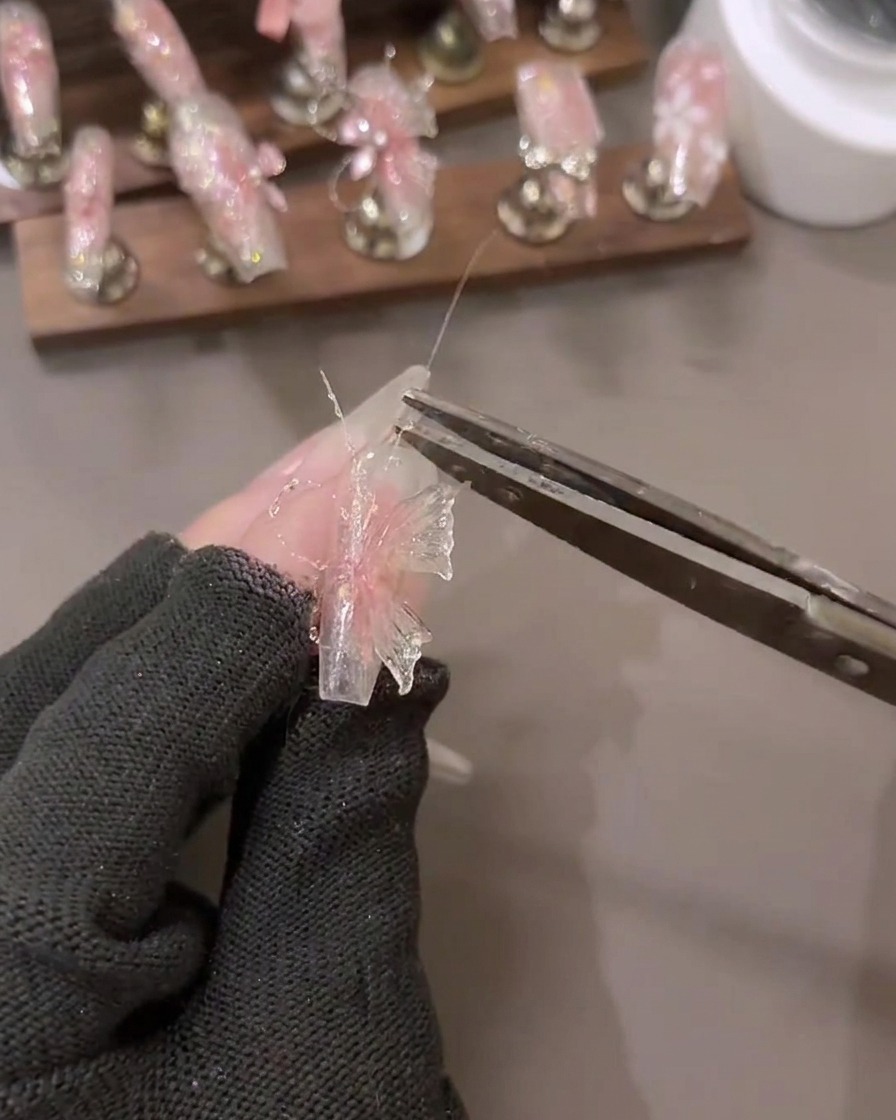 Un primo piano di una mano che applica dettagli in gel glitterato effetto diamante su un design di nail art 3D.