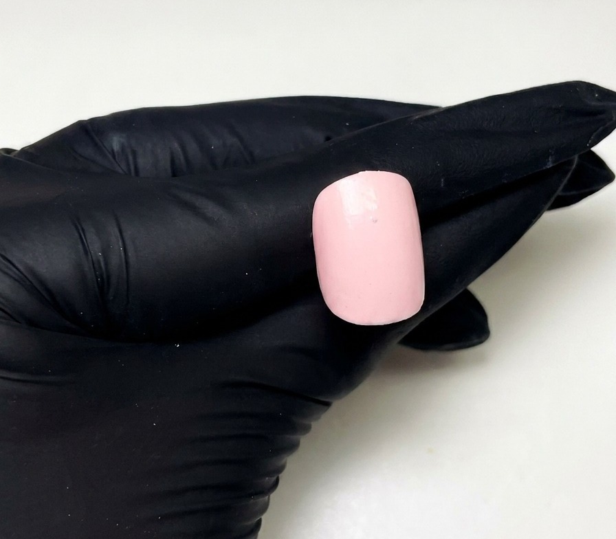 Primo piano di ununghia rosa preparata con un singolo piccolo punto di gel costruttore rosa posizionato nella parte centrale superiore.