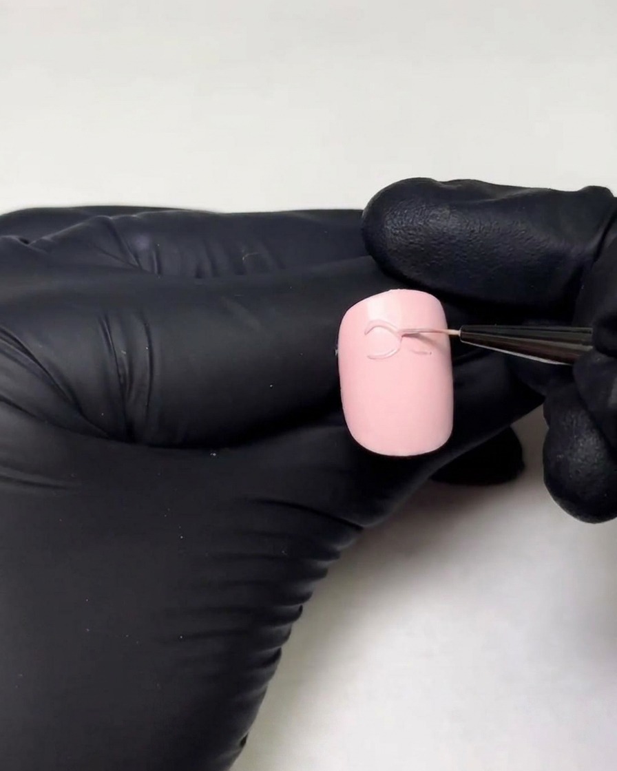 Mani con guanti che disegnano il secondo anello di un fiocco in gel 3D su ununghia usando un pennello liner fine.