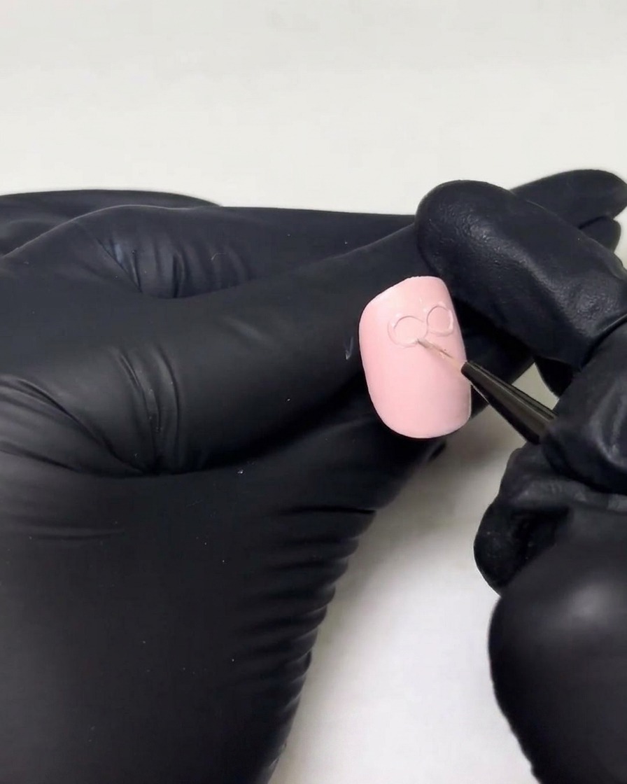 Mani con guanti che aggiungono uno strato più spesso di gel costruttore sugli anelli esistenti di un design con fiocco 3D su ununghia.