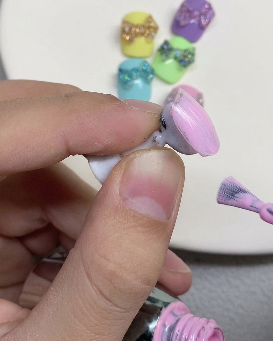 Un pennello per unghie che applica uno smalto gel rosa pastello sulla superficie di ununghia finta esposta su un supporto.