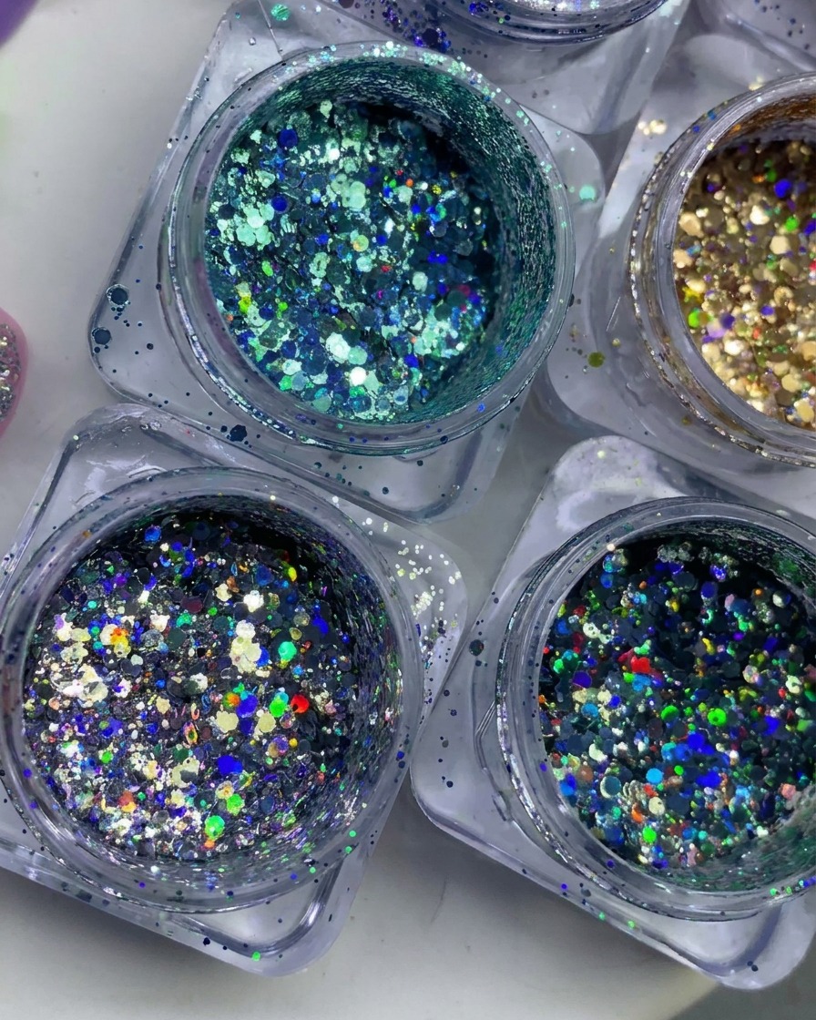 Vista dallalto di numerosi barattolini pieni di scaglie di glitter colorati, olografici e metallizzati.