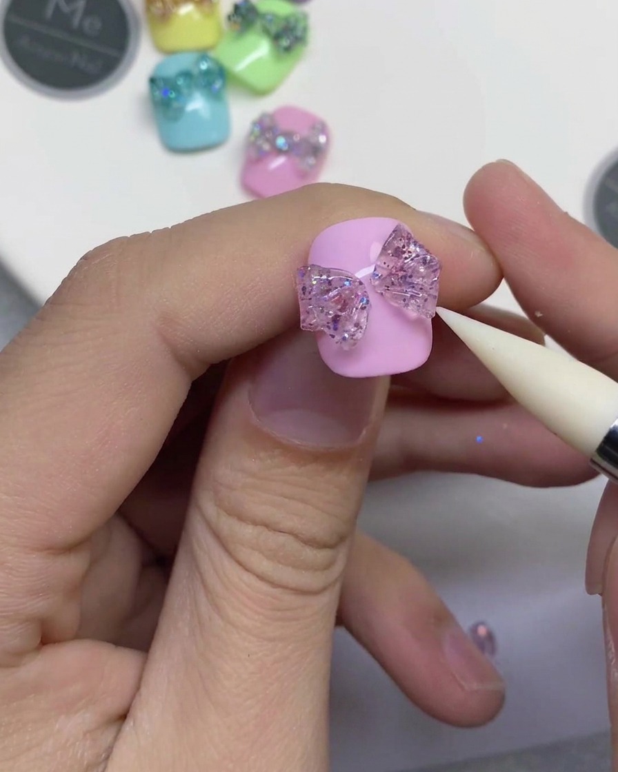Primo piano di uno strumento in silicone bianco che preme su una striscia centrale di gel glitterato per collegare due lati del fiocco su ununghia rosa.