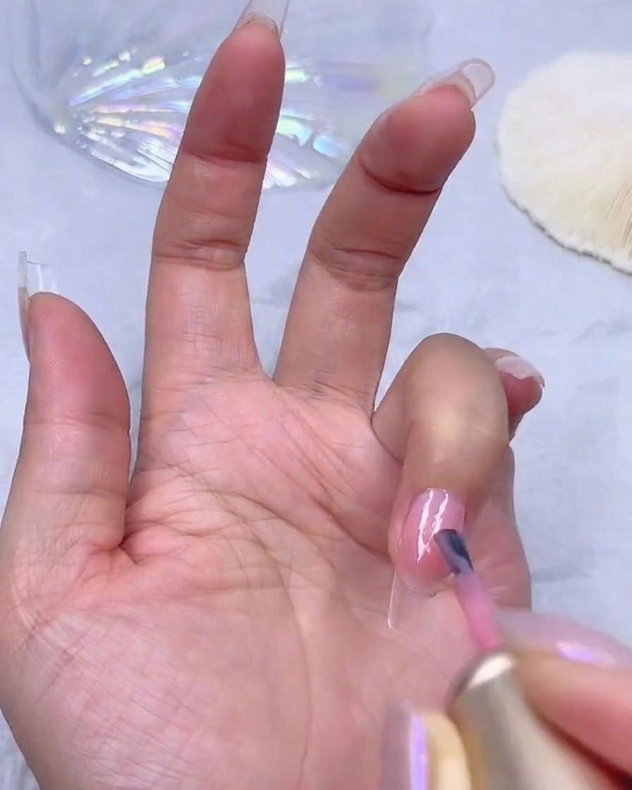 Applicazione di un secondo strato di smalto gel rosa traslucido per aumentare la coprenza del colore sullunghia.