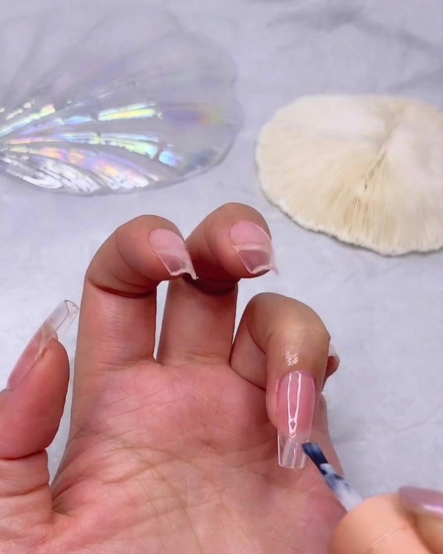 Un pennello che applica uno strato di smalto gel bianco latte sulla punta di ununghia dai toni rosati per creare un effetto ombré.