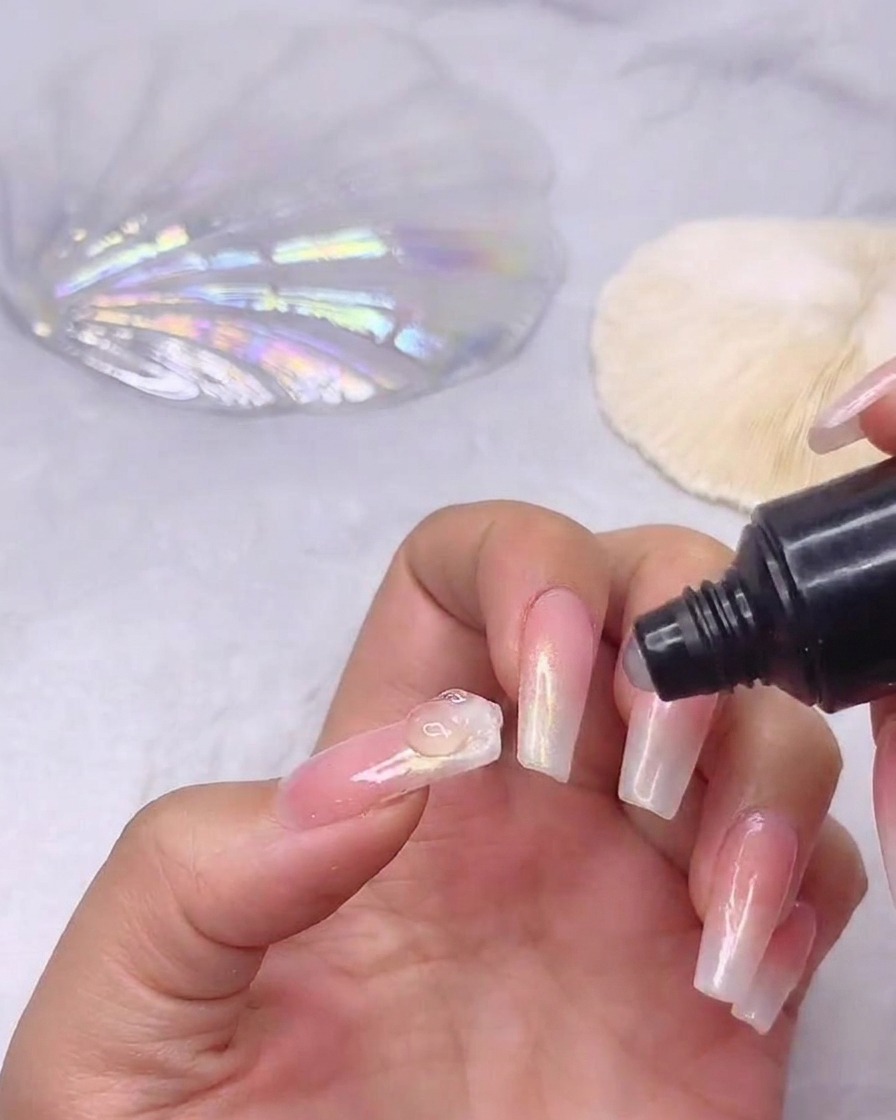 Un tubetto di gel adesivo per strass che eroga una piccola perla trasparente di colla al centro di ununghia sfumata già preparata.