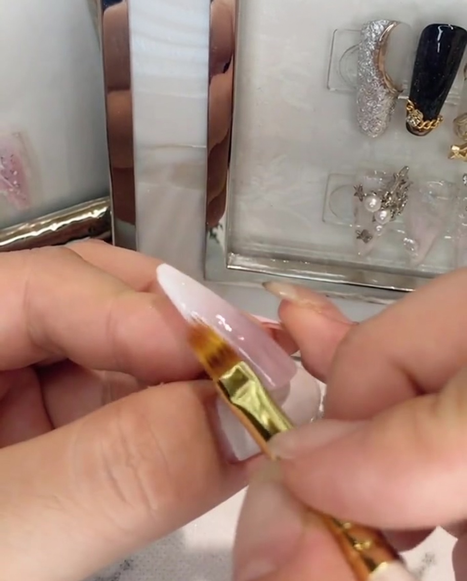 Un pennello che applica il top coat trasparente su ununghia ombré rosa e bianca.