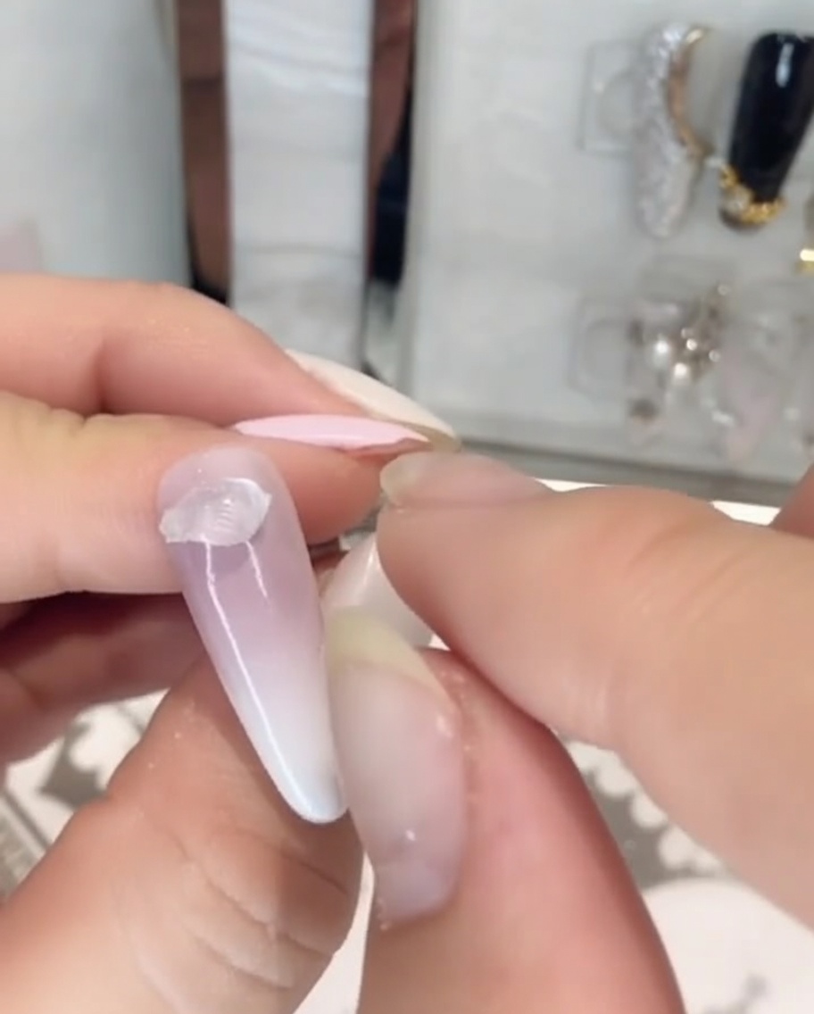 Dita che posizionano un pezzo di colla per strass solida, trasparente e densa sulla base di ununghia dipinta.