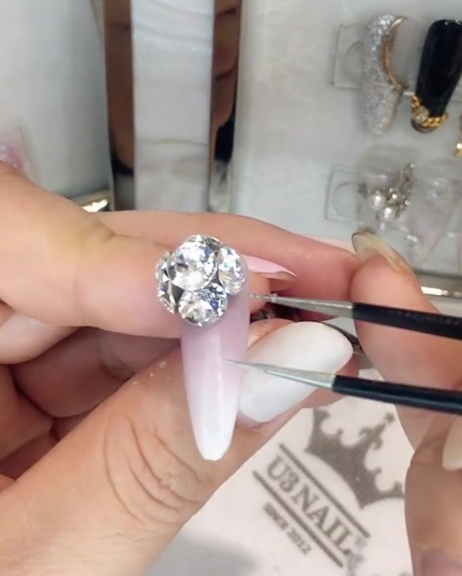 Un paio di pinzette di precisione che regolano i singoli cristalli in un grande cluster di strass su ununghia.