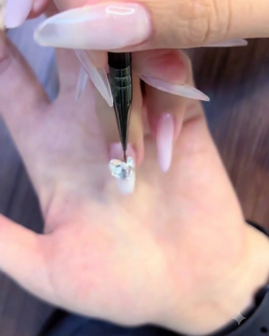 Un pennello sottile per nail art che posiziona minuscoli strass rotondi lungo i bordi inferiori di un grande grappolo di cristalli.