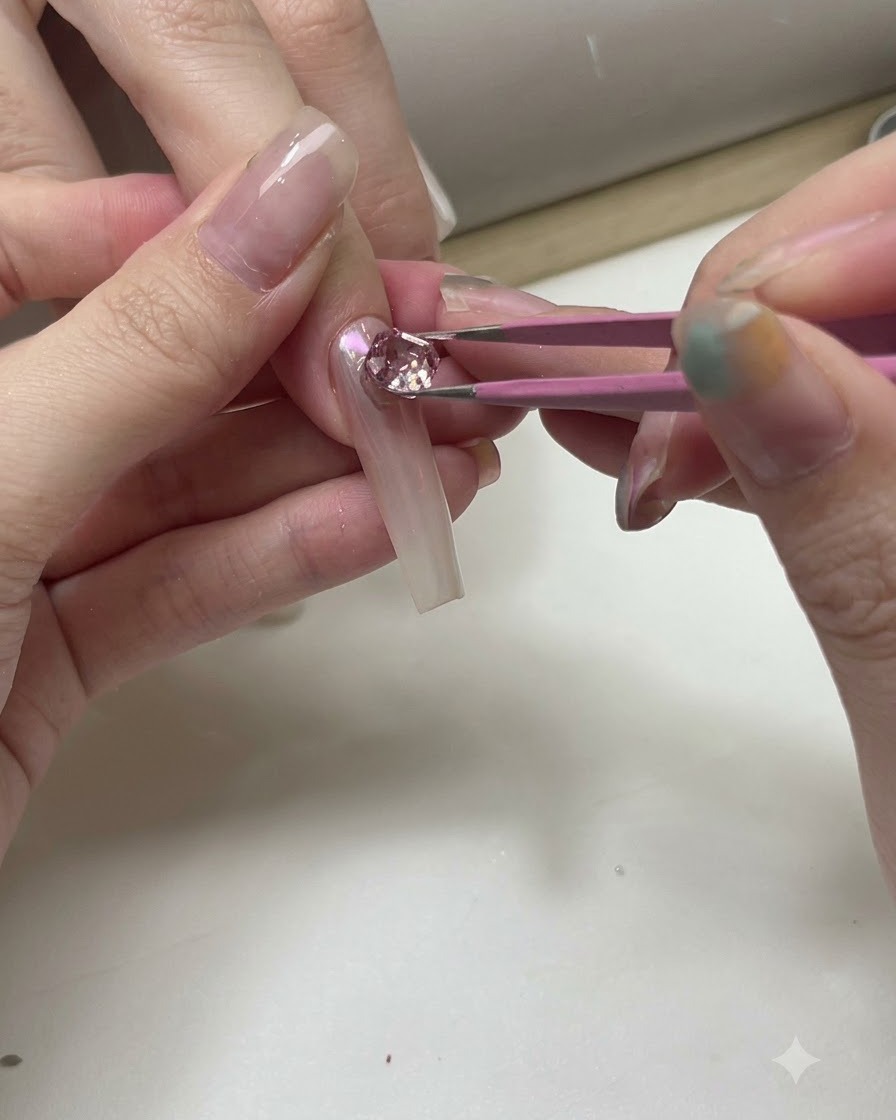 Una pinzetta che posiziona cristalli scintillanti rosa e trasparenti su una tip trasparente per prove di nail art.