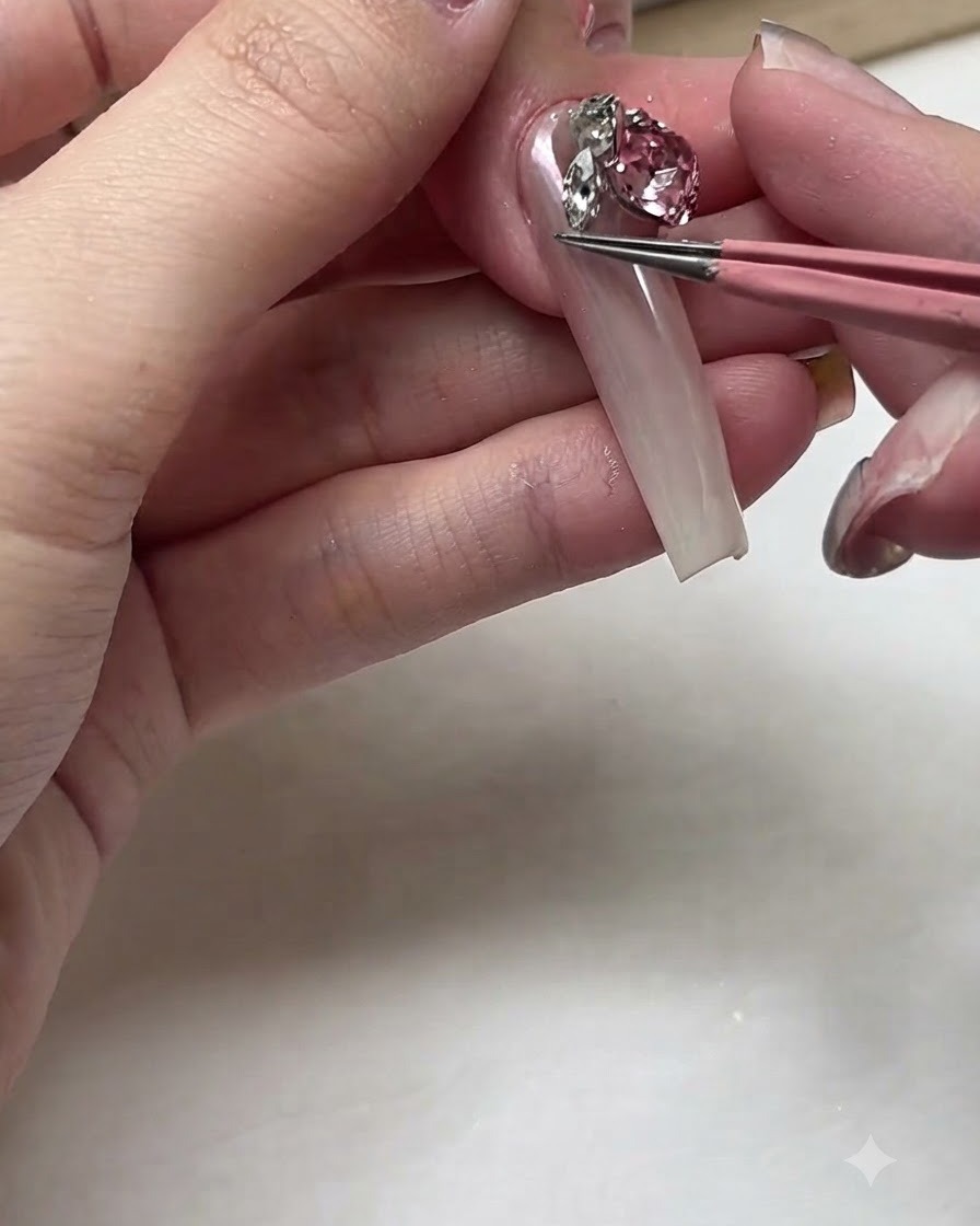 Un paio di pinzette rosa che posizionano un grande strass in cristallo rosa brillante su un letto ungueale lungo.