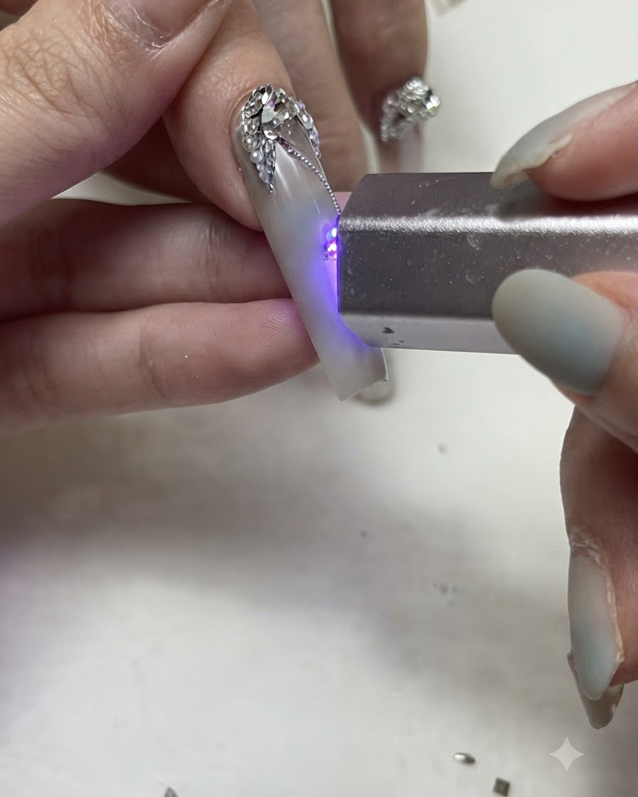 Una torcia di polimerizzazione UV/LED portatile che polimerizza linee fini in gel argentato e dettagli in strass su ununghia decorata.