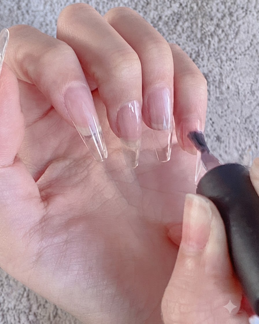 Un pennello da unghie che applica una mano di smalto semipermanente scuro su unestensione per unghie trasparente.