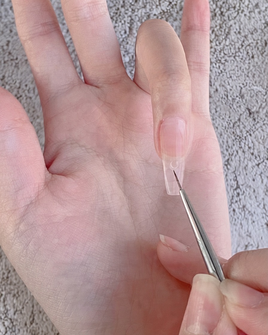 Un pennello liner fine per nail art che posiziona una piccola goccia trasparente di gel per strass su ununghia rivestita di gel nude.