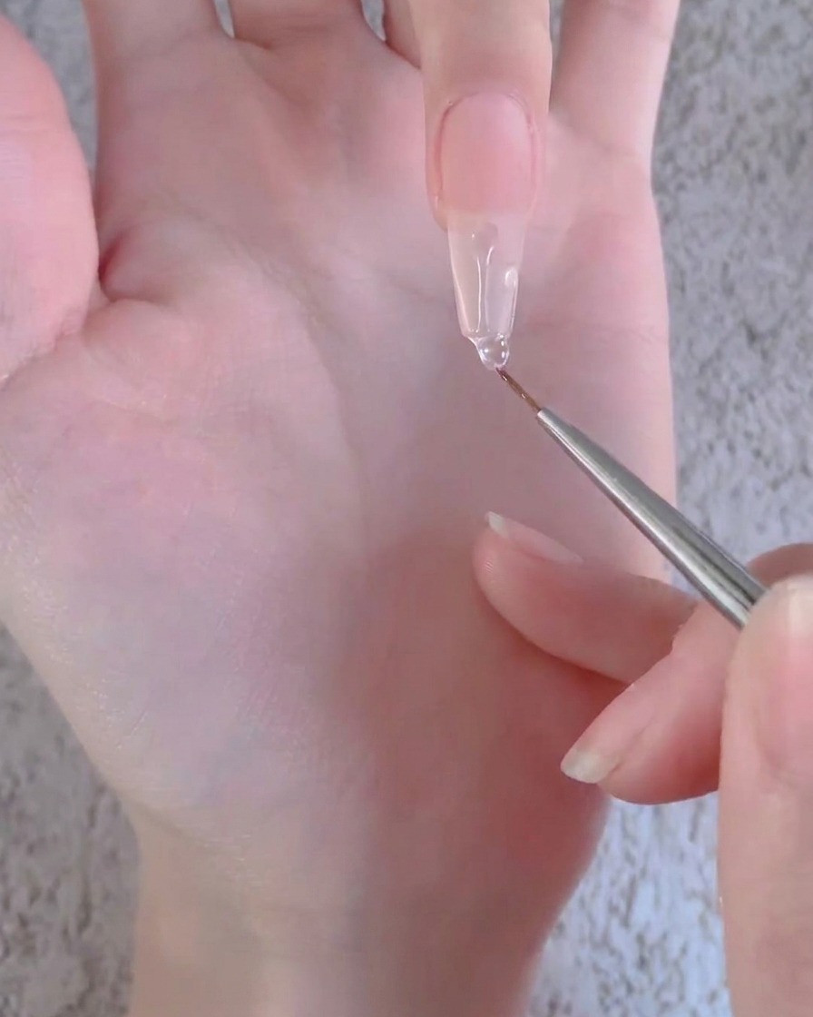 Un pennello liner che tira una goccia di gel trasparente verso il basso lungo la lunghezza di unestensione per unghie artificiali lunga.