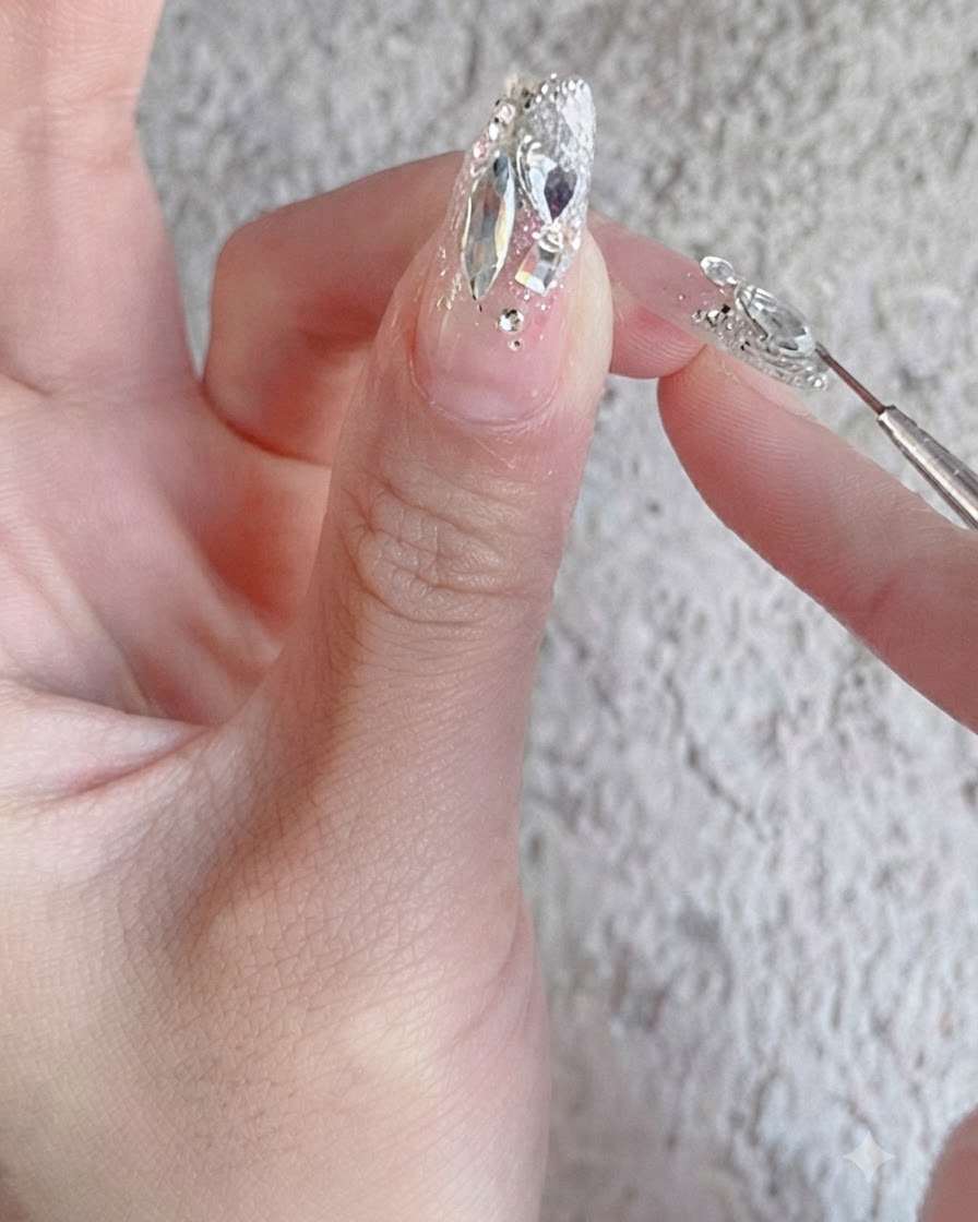 Un pennello da unghie che applica un top coat di rinforzo lucido su un design di unghie con strass completamente rifinito.