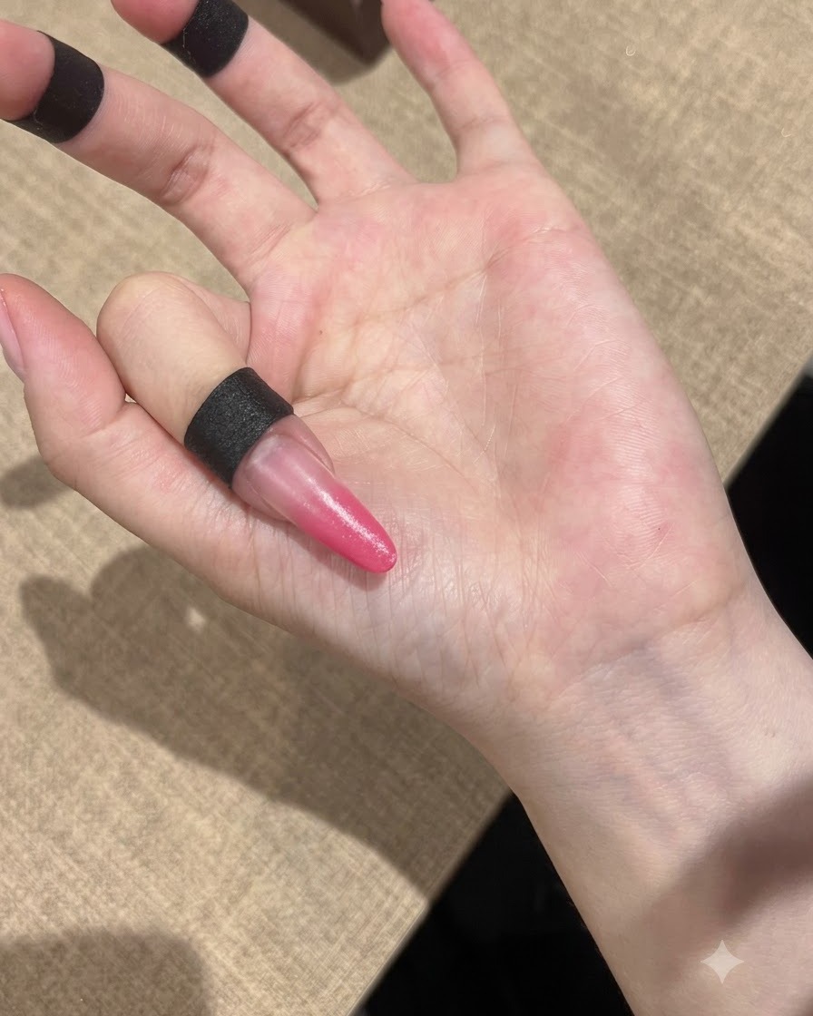 Una mano posizionata sotto una lampada UV compatta per polimerizzare le unghie sfumate di rosa.