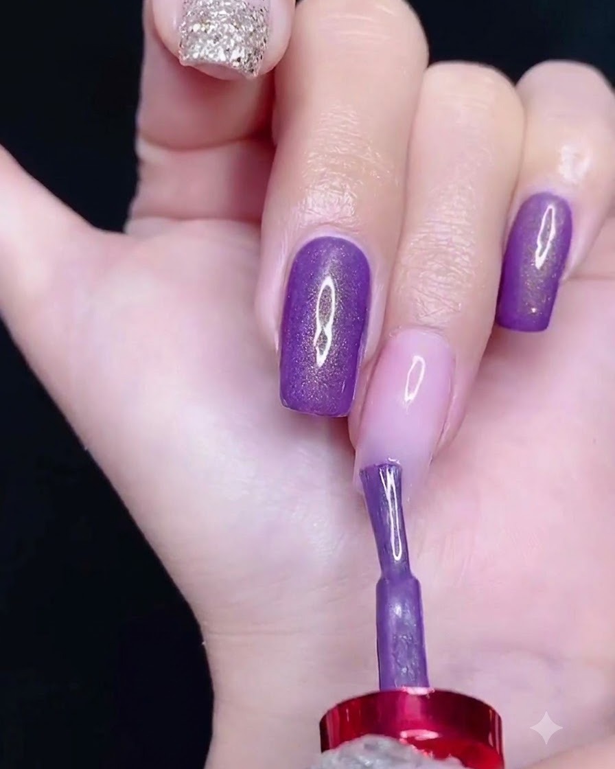 Un pennello che applica lo smalto gel viola sulla parte superiore di ununghia.