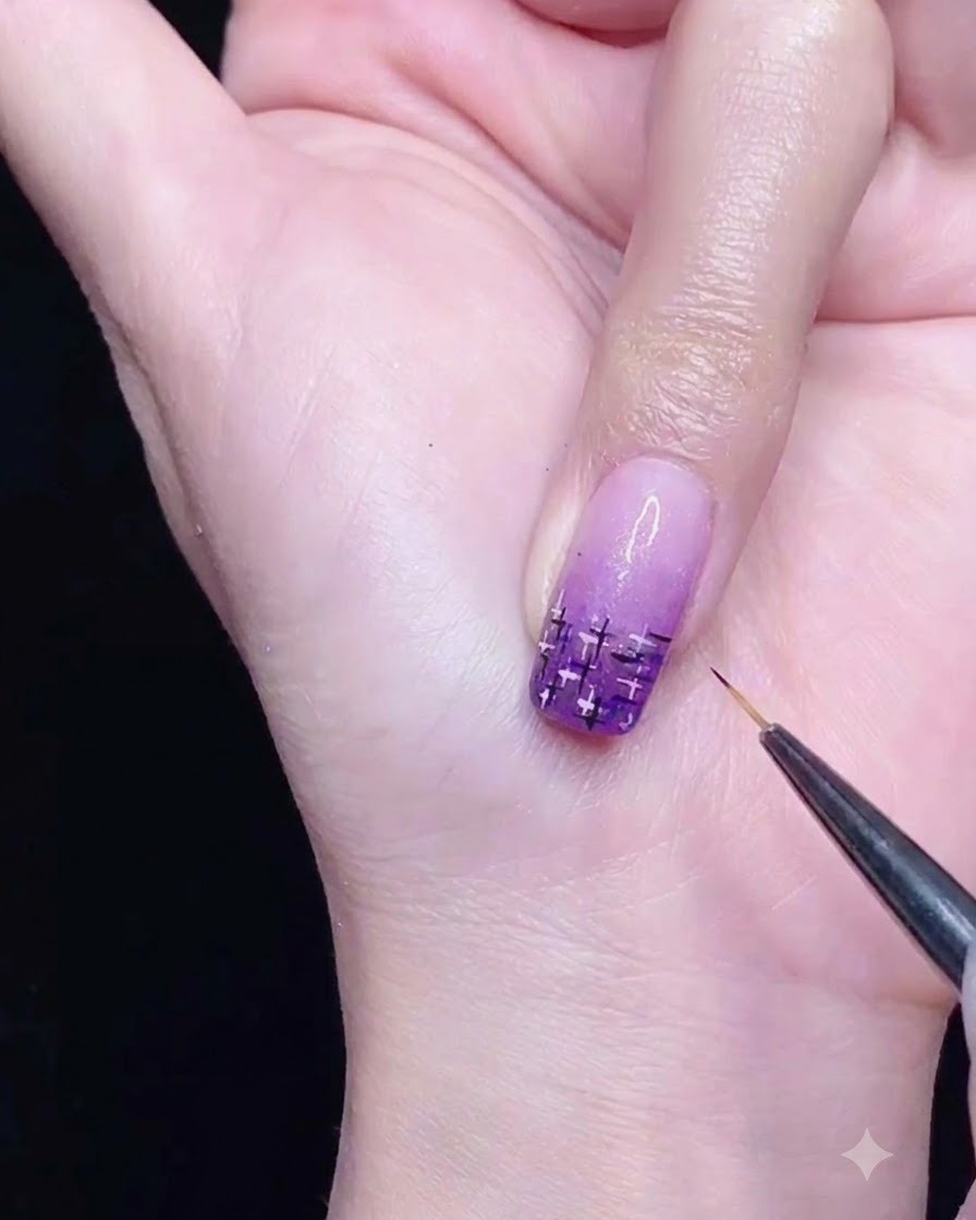 Un pennello liner sottile che disegna linee intersecanti nere e argento su ununghia con sfumatura viola.